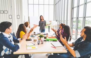 Multiethnic diverse group of creative team or business coworker clapping hands in project presentation meeting leading by Asian woman. Success teamwork, modern office work, or startup company concept